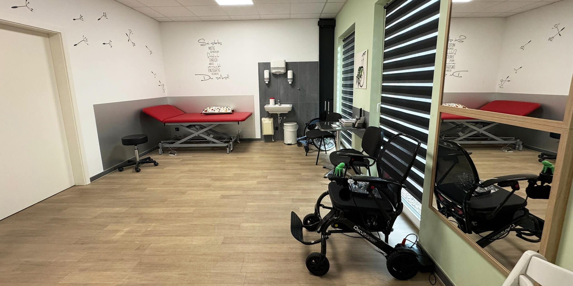 Therapie- und Anpassungsraum mit Rollstuhl, Spiegelwand und Untersuchungsliege